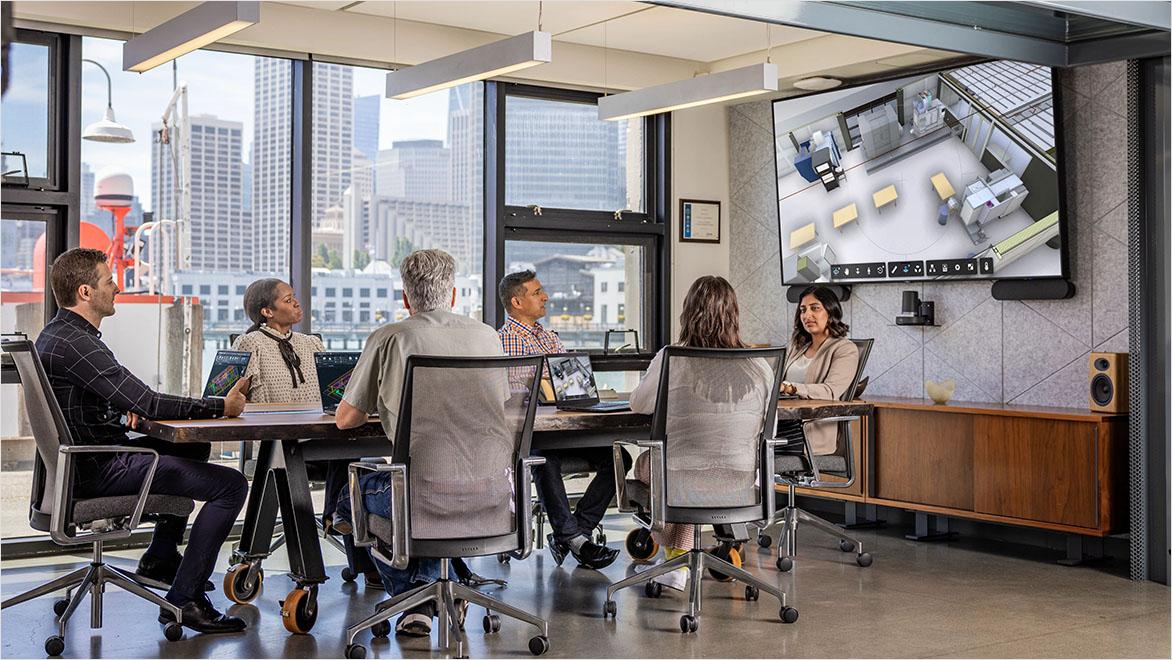 Architects sit at a conference table, looking at a building interior rendering onscreen.