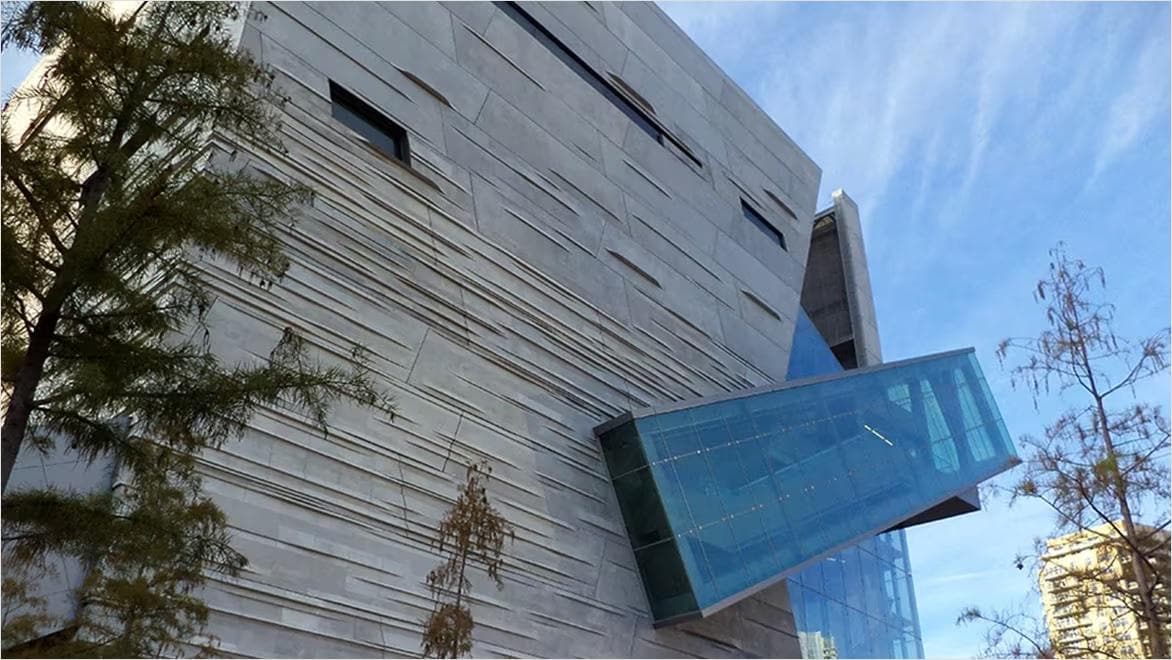 A modern concrete building facade showcases a dramatic diagonal window.