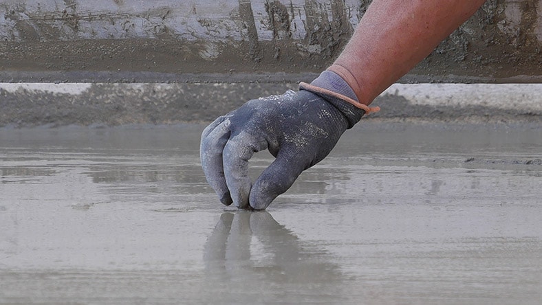 The hand of a construction worker is shown smoothing concrete.