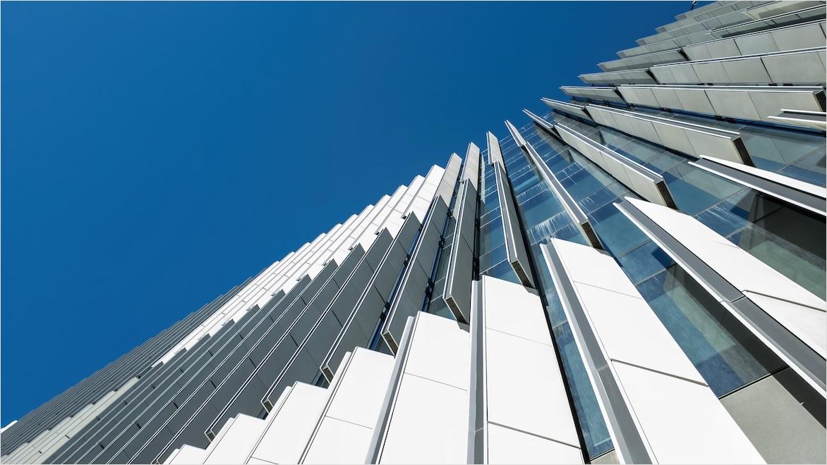 Upward view of a tall modern office building exterior showing adjustable external slats to control incoming natural sunlight for internal light and temperature control.