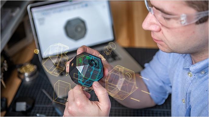 A man holds a small camera device in front of a laptop showing the device’s design; a graphic overlay shows an exploded view of the device’s components.