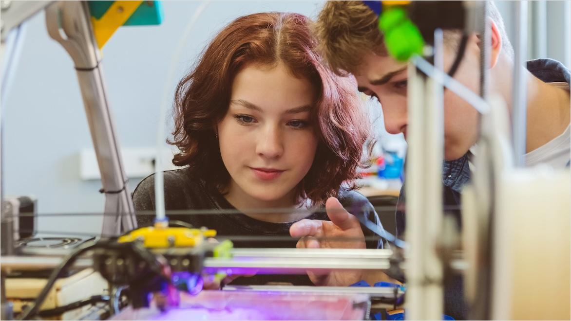 Two students watch a 3D printer in action.