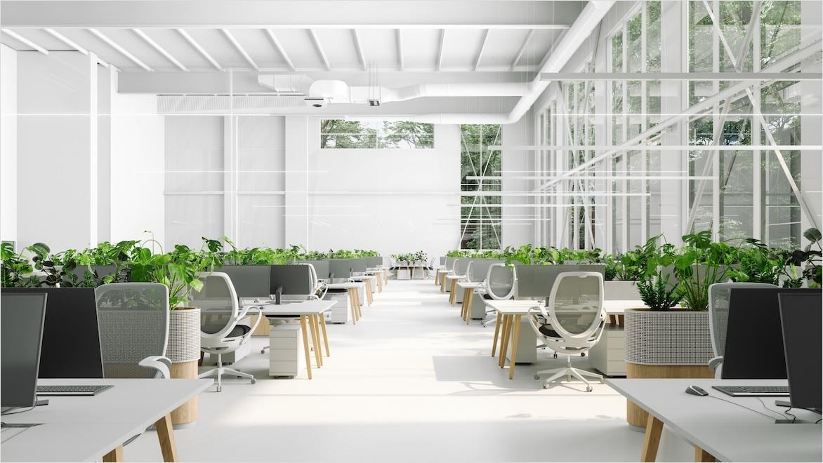 An eco-friendly open-plan office interior shows tables, chairs, windows, and plants.