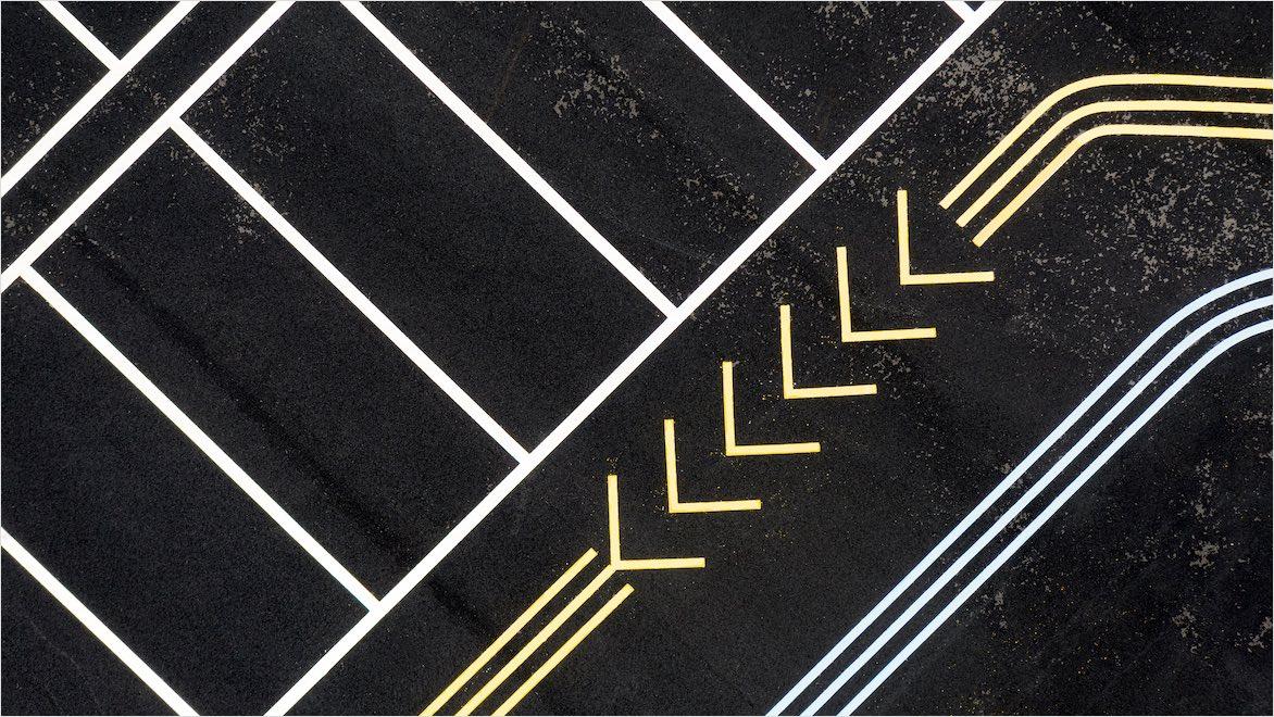 An overhead drone photo of a parking lot shows spaces and arrows guiding vehicle flow.