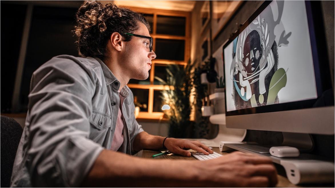 A young man works on a desktop computer whose monitor displays a graphic drawing.