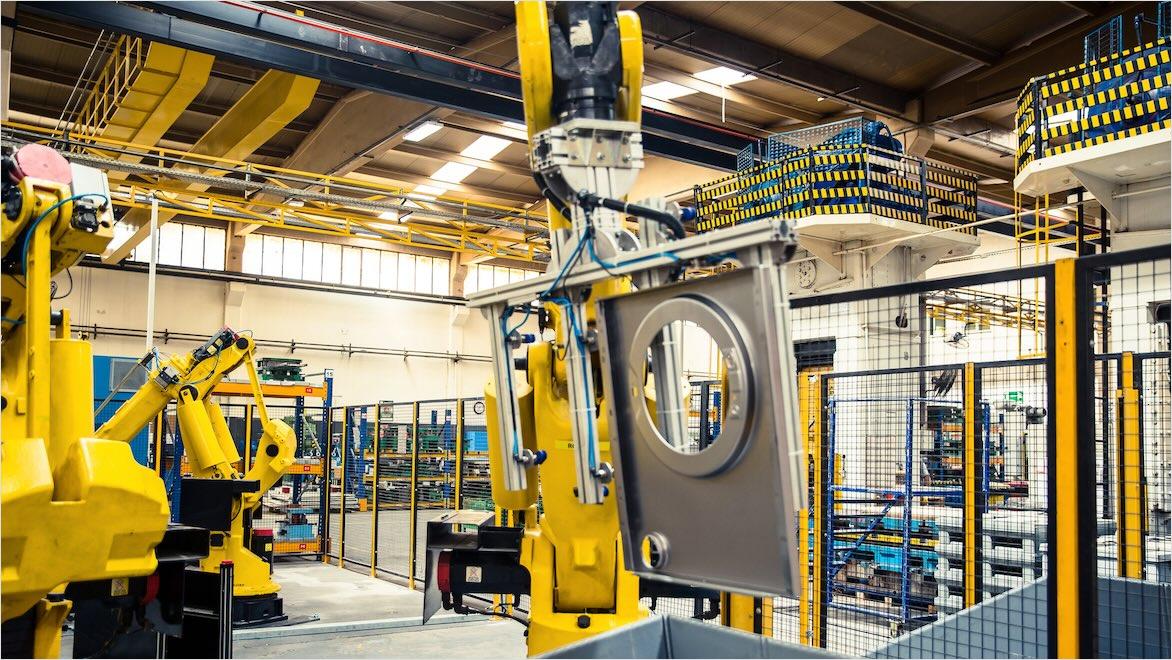 A robotic arm in a modern factory lifts a washing machine door.