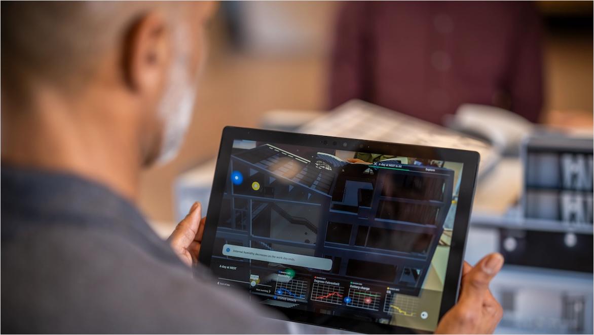 A man views a tablet displaying building data. A building model is in the background