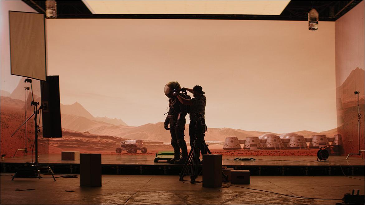 一位宇航员装扮的演员站在电视机前。