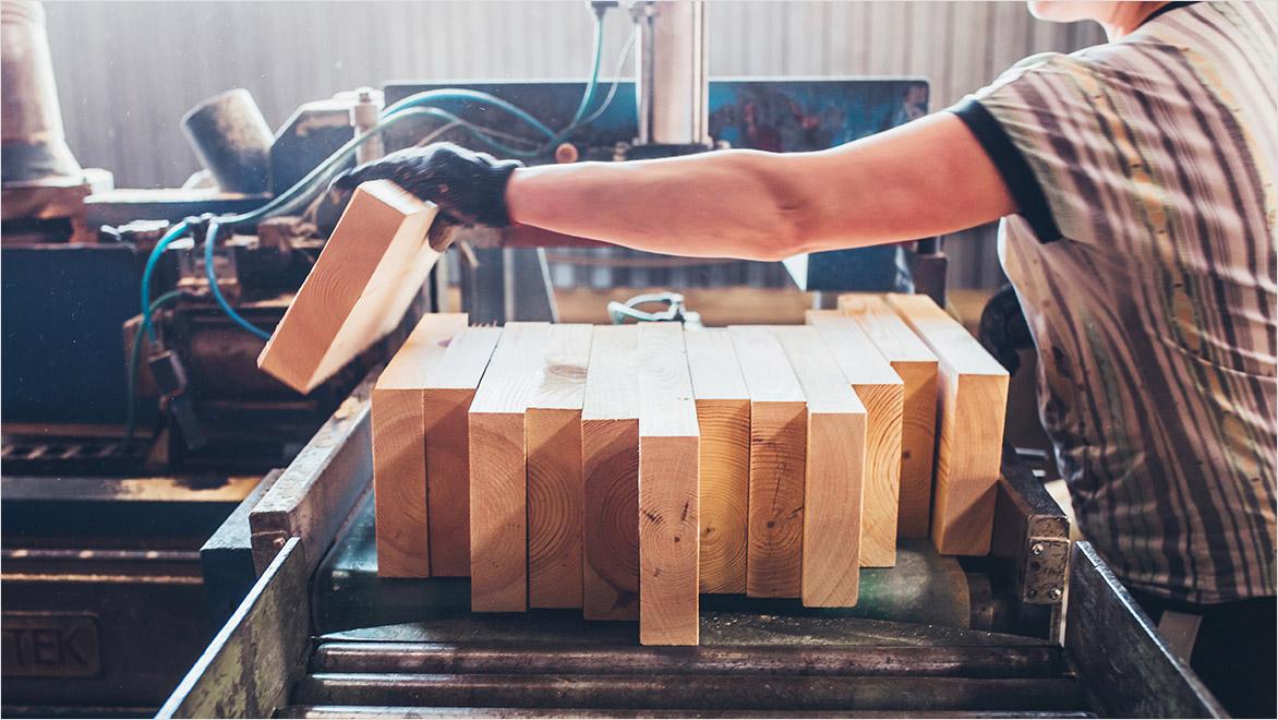 A woodworker aligns pieces of wood on a machine that creates glulam.