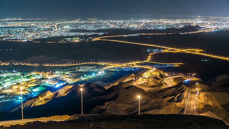 A photograph of Jebel Hafeet mountain at night shows Abu Dhabi in the distance.