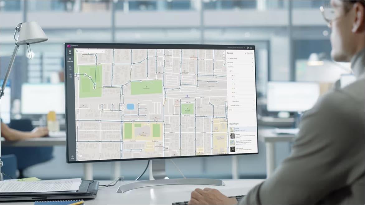 A computer monitor shows a screen from Autodesk Info360 Asset mapping water systems under a grid of city streets.
