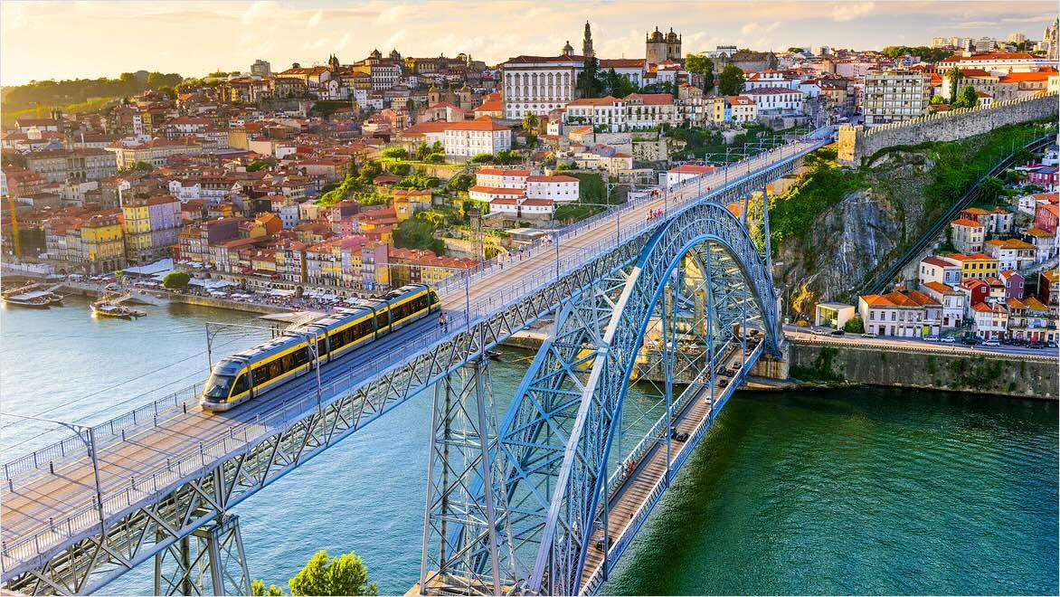 A modern train is shown traveling across a bridge with a cityscape in the background.