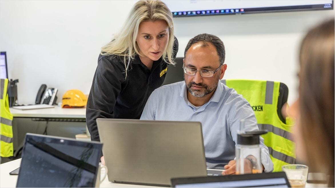 A man and woman look at a laptop computer in a construction office.