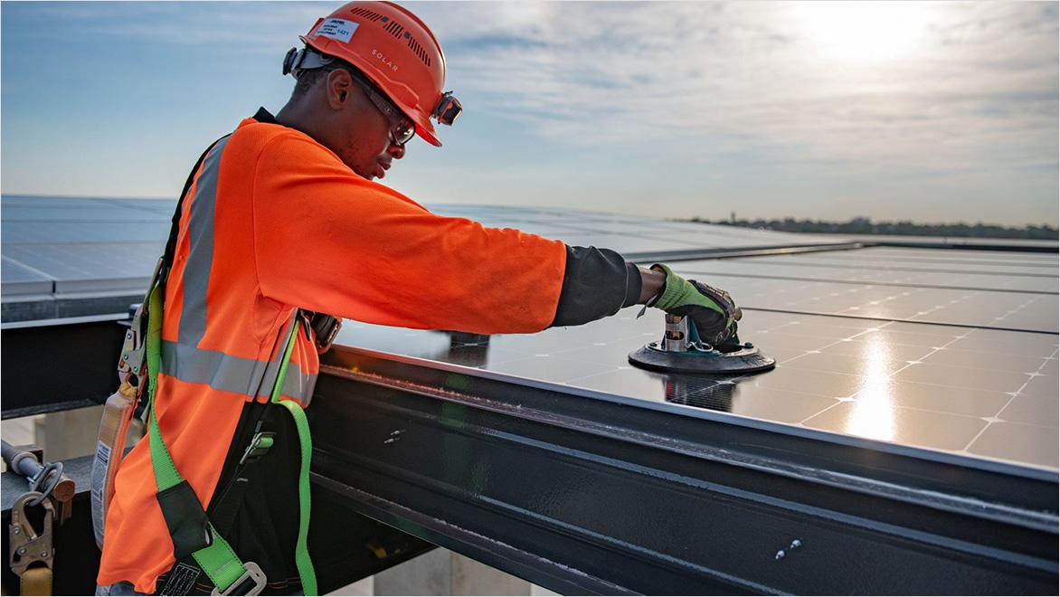 A worker installs solar panels on a building.