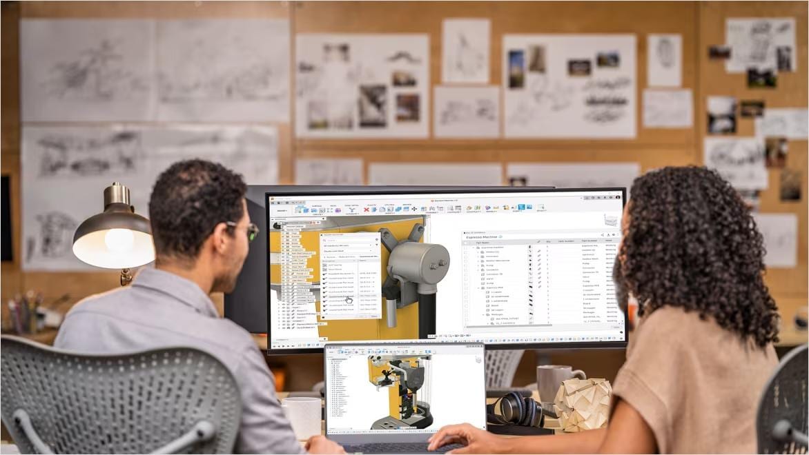 Two product designers in an office work together in front of computer screens showing CAD software.