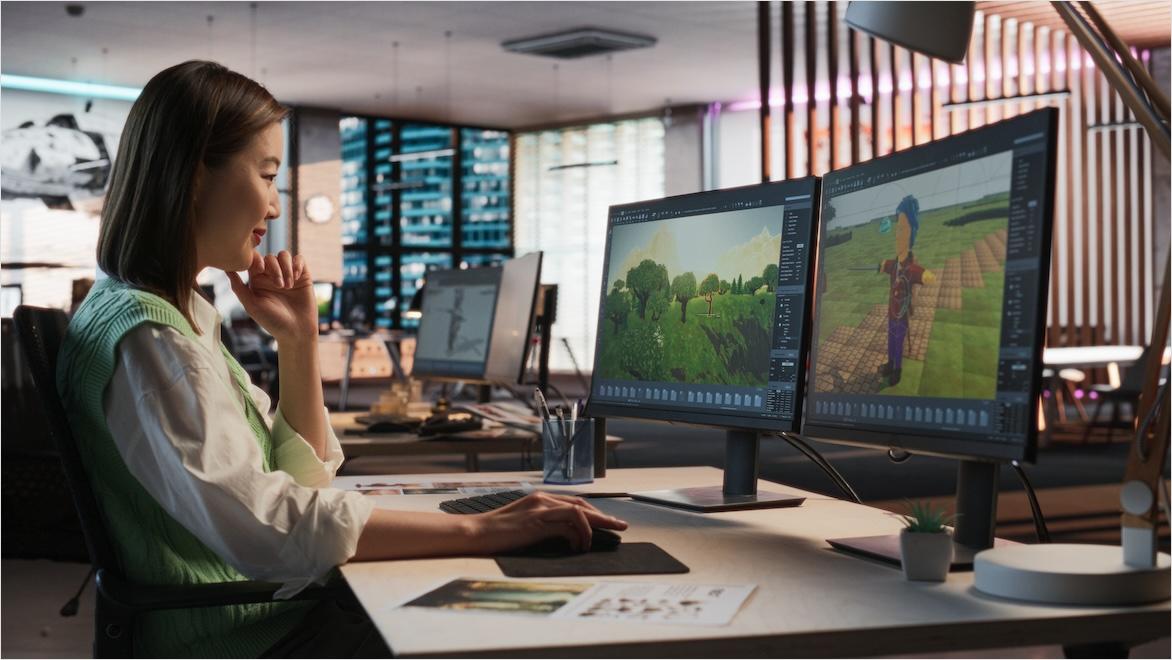 A woman designs video game worlds at a computer workstation.