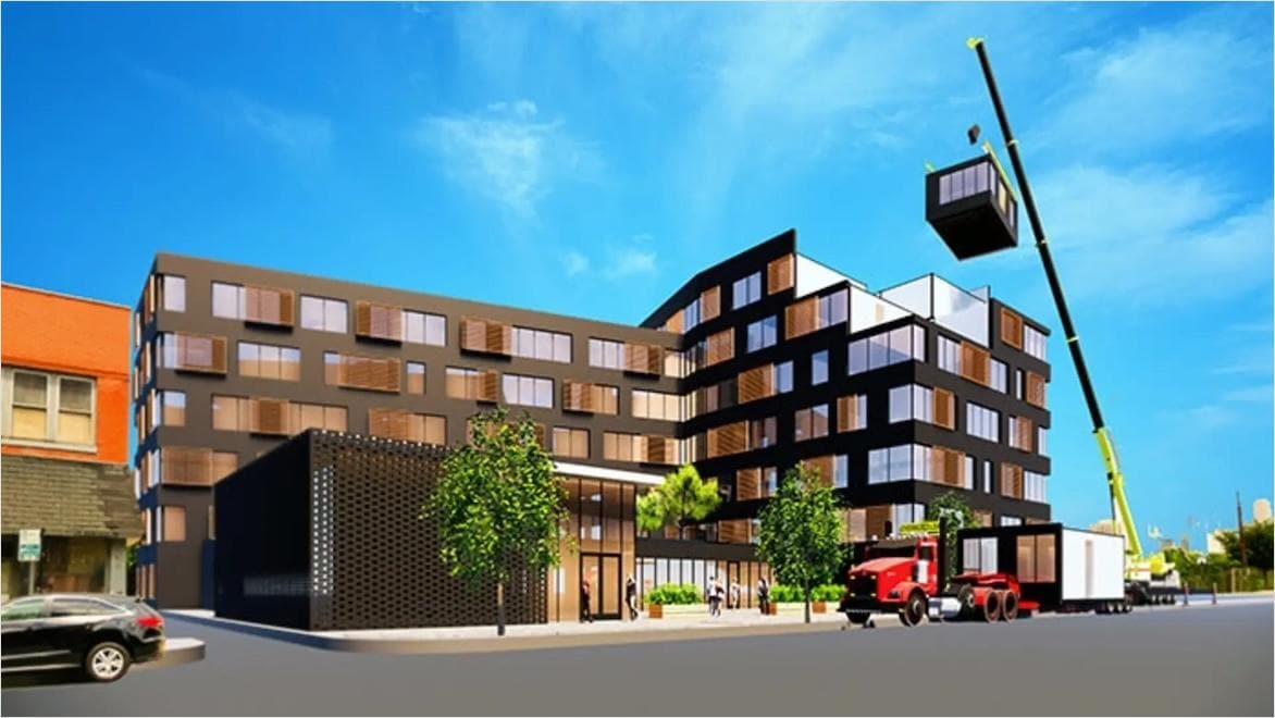 A section of a modular housing complex is lowered into place with a crane.