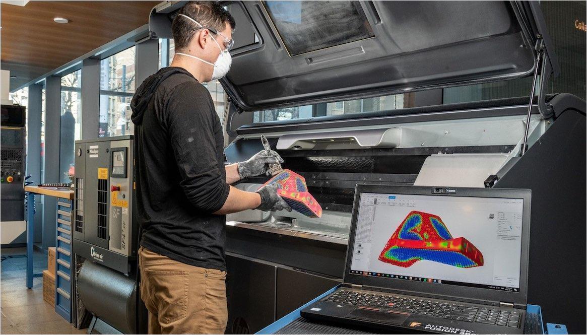 3D 打印机旁的增材制造人员,手持 3D 打印零件,笔记本电脑在前景中显示零件设计