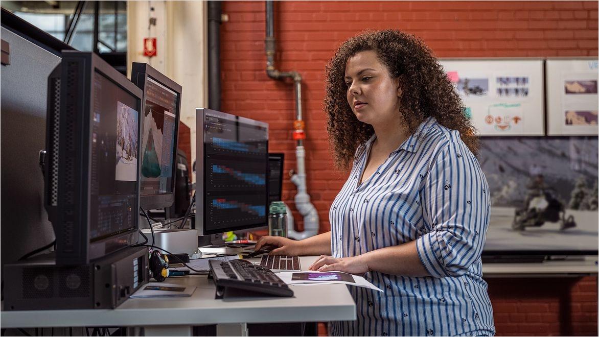 A woman at a standing desk works on a computer displaying film production management software.