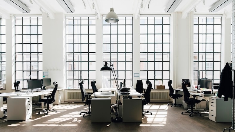A modern office space is flooded with light from floor-to-ceiling windows.