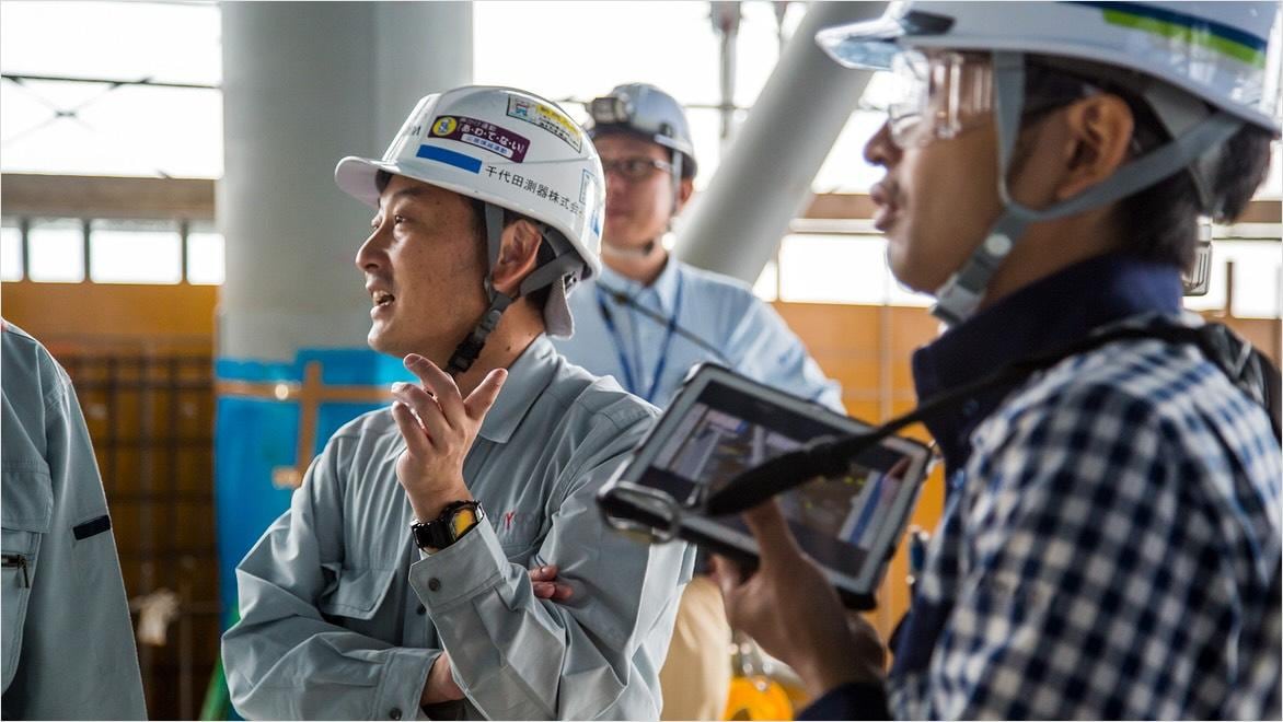 Several people in hard hats have a discussion on a construction site.
