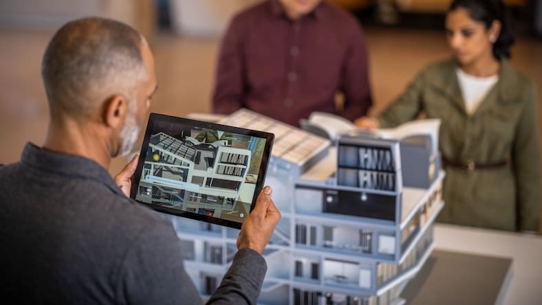 A man views a scale building model through a tablet that overlays architectural information onto the image.