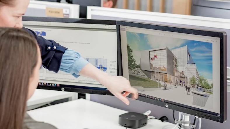Two young women look at a desktop computer monitor displaying a 3D visualization of a building design project.