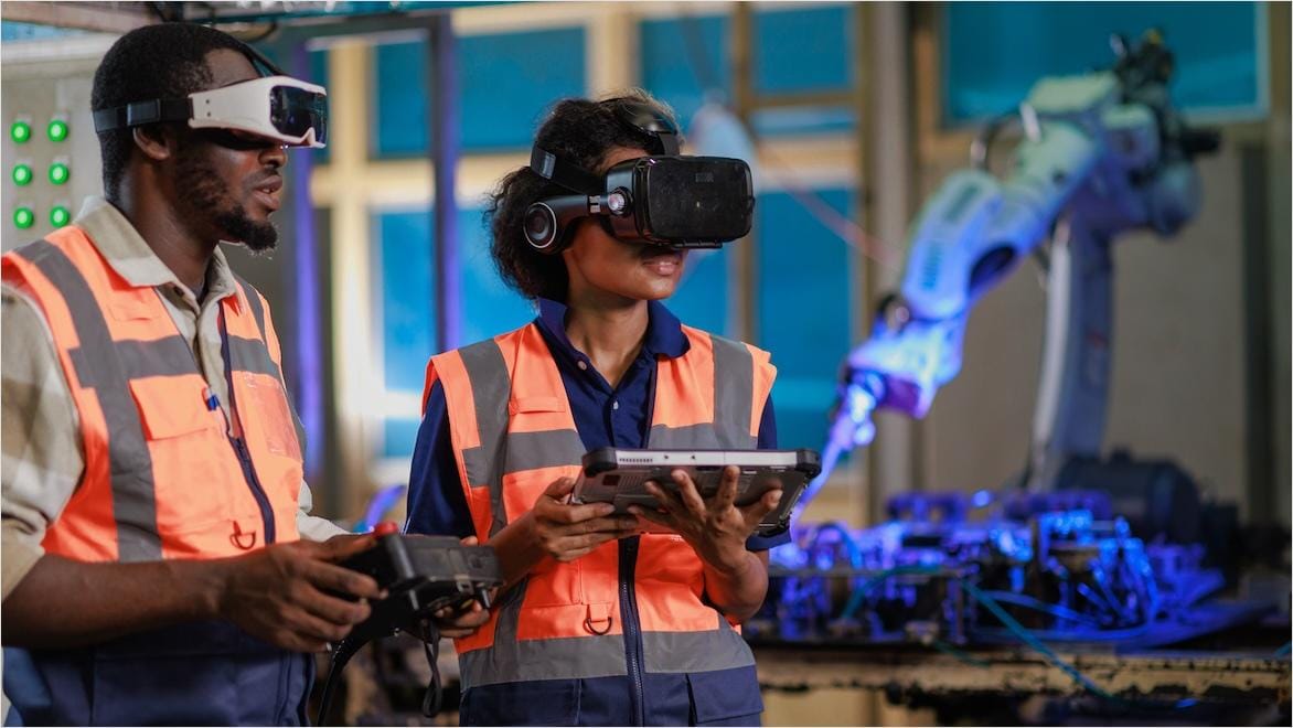Two technicians wearing XR headsets operate a robotic arm in a factory.