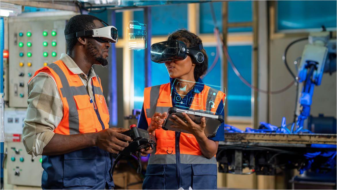 Engineers with tablets and VR headsets controlling robotic arm in factory