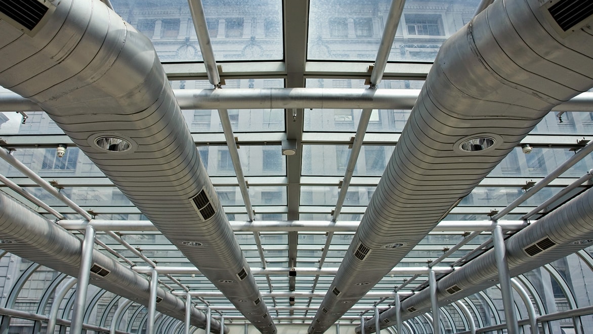 Flat metal HVAC ducts running along glass ceiling in industrial building