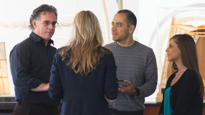 Image shows four professional people standing together engaged in discussion