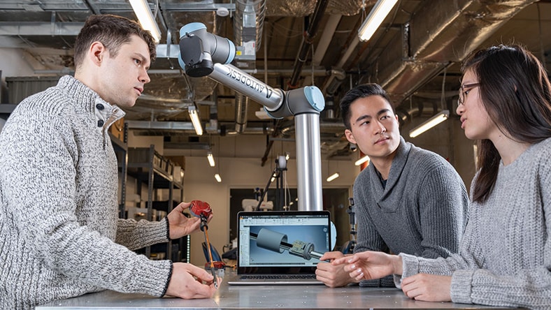 3 engineers standing around a table with a computer and talking