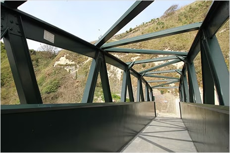 Concrete walking bridge with green overhead trusses