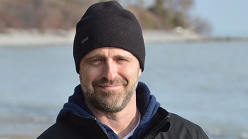 Professor Paul Neale in his home office speaking to a web camera with several guitars mounted behind him
