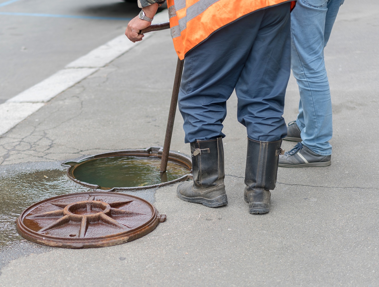 a manhole with lid removed is overflowing. two men are working to fix it.