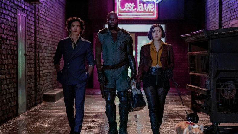 Three people walking through neon-lit alley.