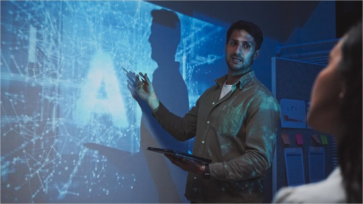 Man presenting in front of screen displaying representation of AI code.