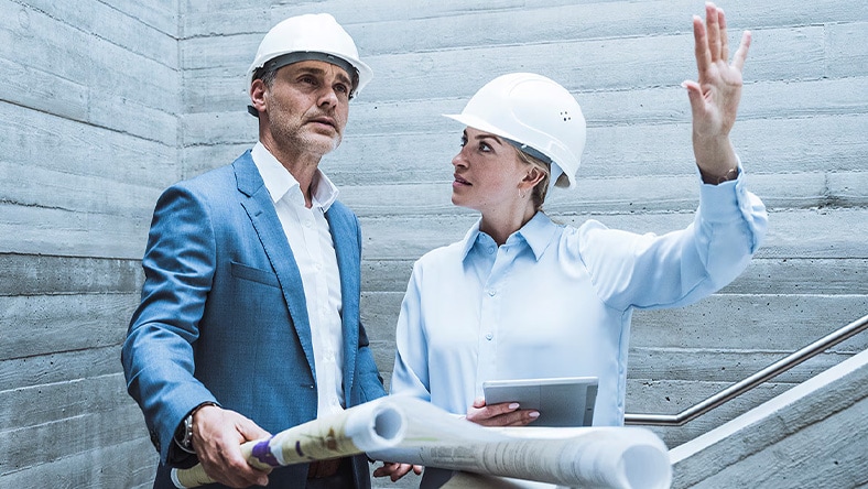 Illustration of two owners or operators discussing a project, one holding a clipboard and the other gesturing toward a building model, with industrial structures in the background.