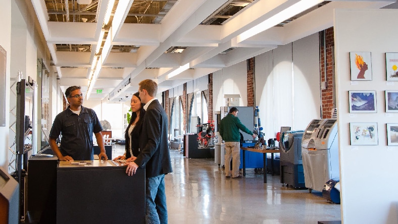 People mill around an exhibit hall that displays different examples of technology.