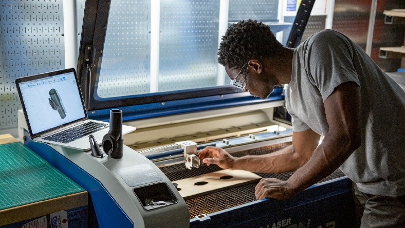 A man in a light-gray t-shirt adjusts a laser-cutting machine.