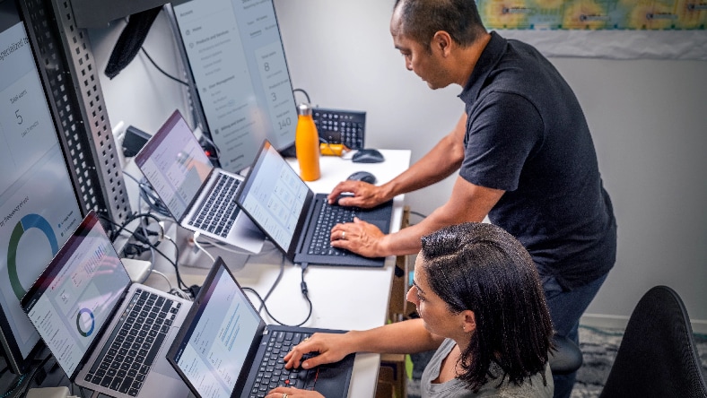 A man and a woman working together on two different laptops in an office environment.