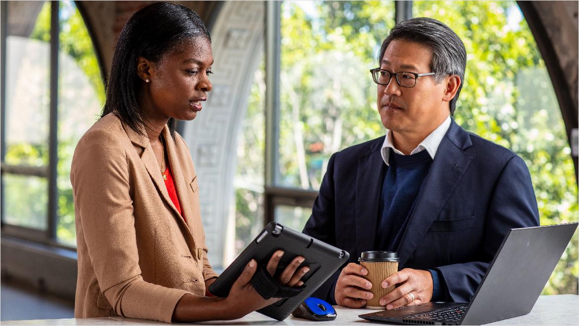 A man and woman standing at a table and reviewing information on a tablet.