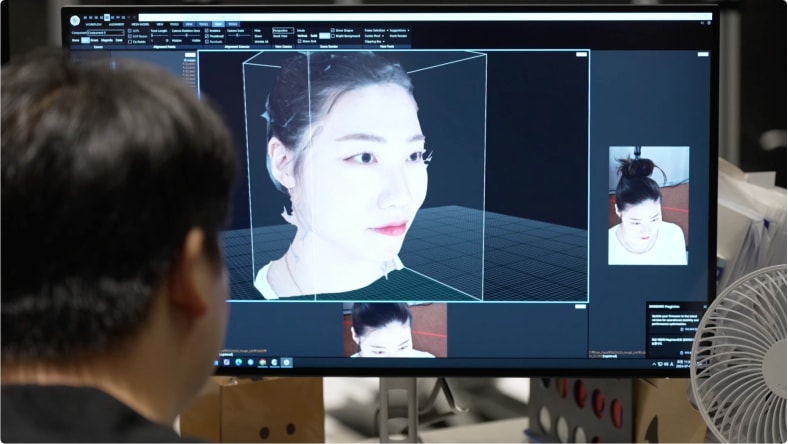 Over-the-shoulder view of a designer working with a 3D rendition of an actor's facial features