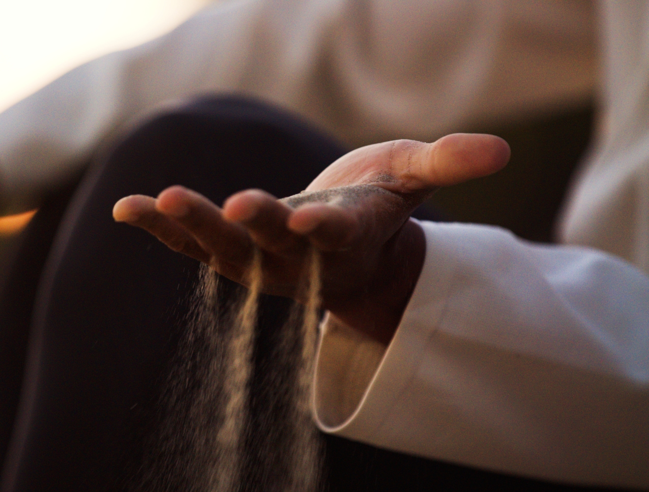 A close-up of a person’s hand held open as fine sand slips through their fingers, captured in warm, soft light.