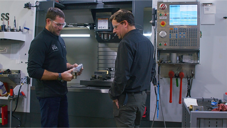 Mike Schultz and Noah Elliott discuss a material part in a design shop. 