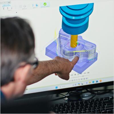 A teacher points to a computer screen showing Autodesk Fusion software for CAD, the image shows only the back of the teacher's head