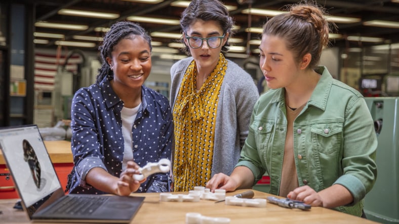 Three women gather around a part prototype produced in Autodesk Fusion