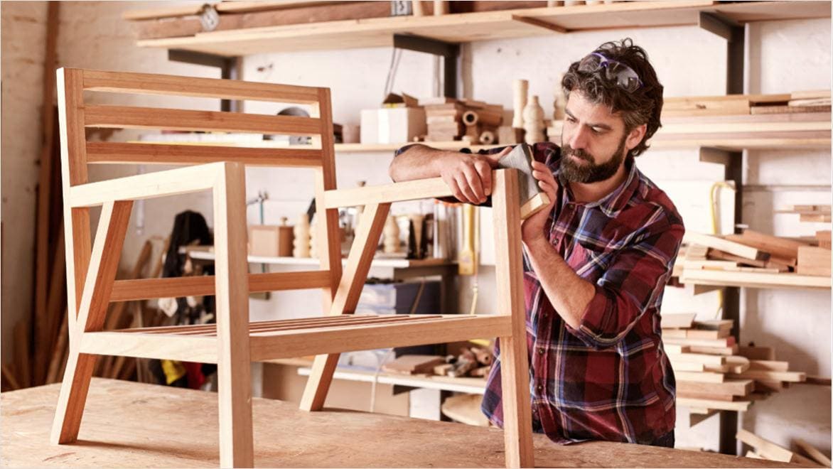 Furniture designer sanding a wooden chair.