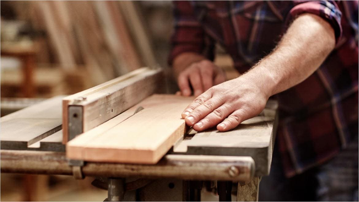 Man cutting a piece of wood with saw for woodworking.