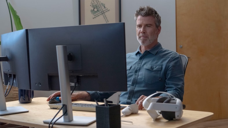 Man looking at computer with VR headset on the desk